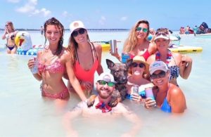 Captain Zander with Bax the Boat Dog on his shoulder surrounded by women in bikinis at Islamorada Sandbar on Independence Day