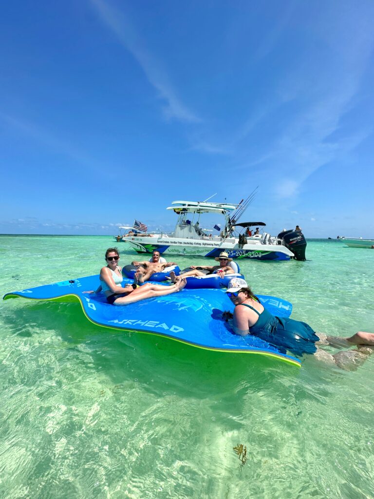 Group of happy guests floating on a lily pad at Islamorada Sandbar with the Lightly Salted Charters boat in the background