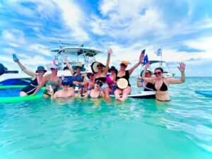 A group of happy people standing in shallow water at the Islamorada sandbar, with the Lightly Salted Charters boat in the background.